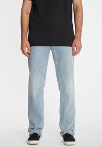 Jeans de mezclilla azul claro con un diseño de pierna recta, con un acabado desgastado y bolsillos estándar, combinados con zapatos negros.