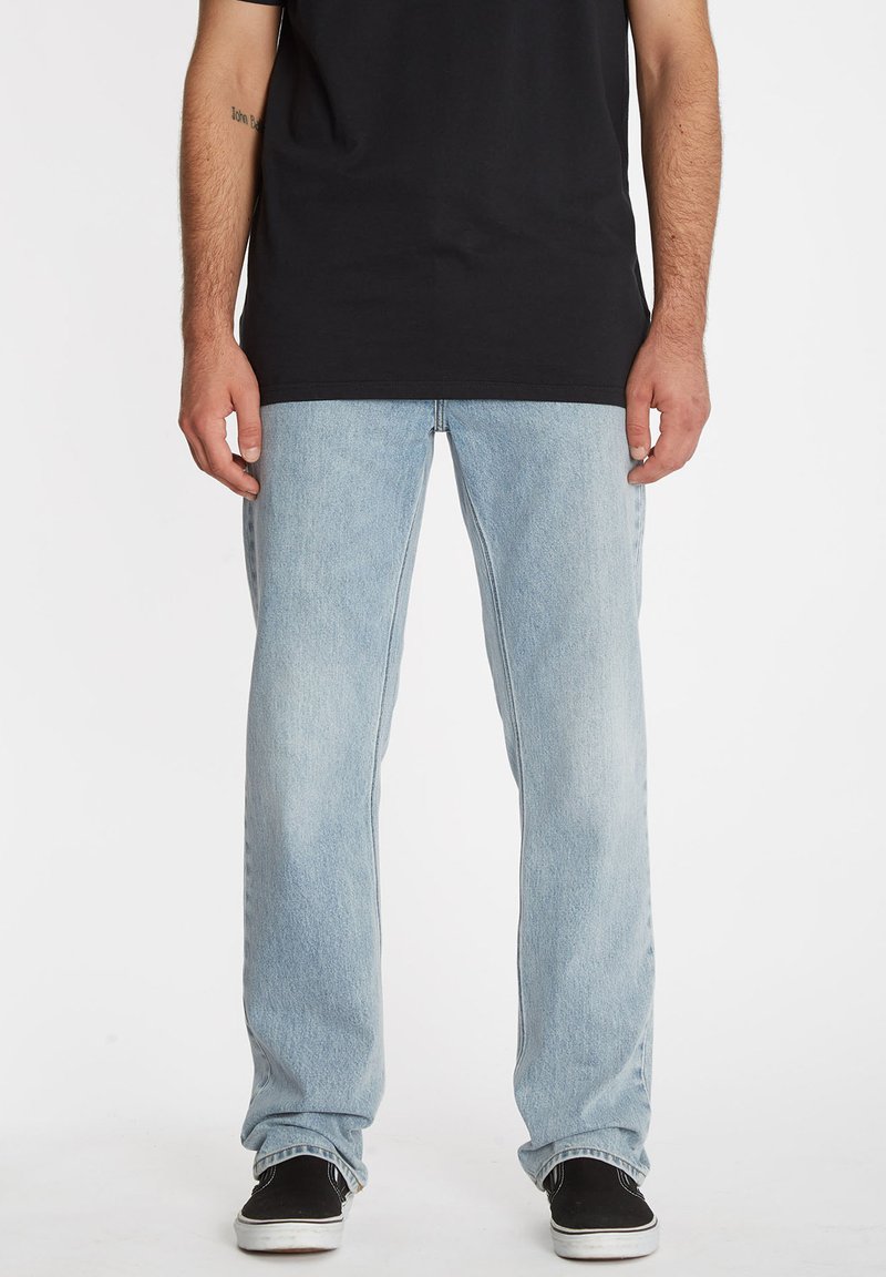 Jeans de mezclilla azul claro con un diseño de pierna recta, con un acabado desgastado y bolsillos estándar, combinados con zapatos negros.