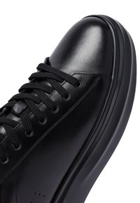 Sneaker in pelle nera con suola in gomma spessa, lacci neri e finitura liscia sulla punta e sulle sezioni superiori.