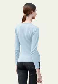 Haut à manches longues bleu clair en matériau doux, au design ajusté, avec un col rond et une texture lisse. Complété par un jean noir.