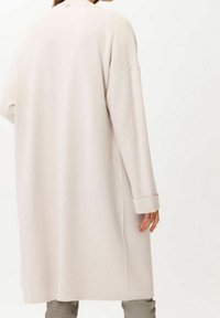 Długi, jasnobeżowy kardigan o luźnym kroju, opadających ramionach i mankietach. Miękka faktura i minimalistyczny design.