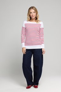 Chemise à rayures rouges et blanches à manches longues associée à un jean ample bleu marine et des chaussures rouges. Tissu doux, coupe décontractée et encolure ronde.