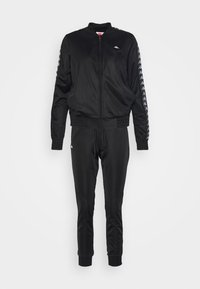 Ensemble veste zippée noire et pantalon, avec logo blanc sur la poitrine, rayures à motifs le long des manches, et poignets élastiques aux manches et aux jambes du pantalon.