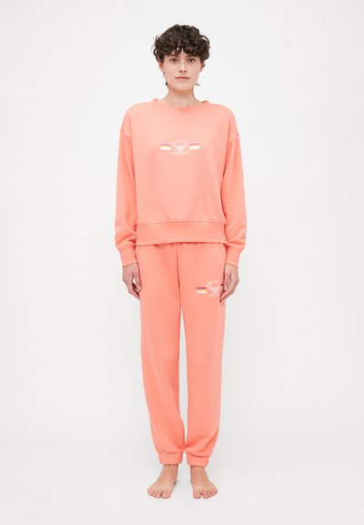 Set de loungewear roz, realizat din bumbac moale. Include un hanorac cu guler tip crew și un logo, împreună cu pantaloni jogger asortați, cu manșete elastice.