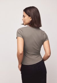 Grå tætsiddende t-shirt med korte ærmer, lavet af et glat stof. Modellen står med ryggen til, hvilket afslører en buet kant og et enkelt design.