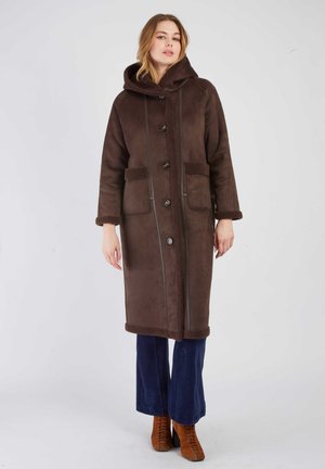 Bruine wollen jas met een capuchon, voorzien van een knoopsluiting, twee voork pocketen, gestructureerde afwerking en een lange snit, gecombineerd met blauwe corduroy broek.