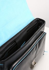 Borsa in pelle nera con interno blu e dettagli in metallo, dotata di più scomparti per l'organizzazione e una chiusura a scatto metallica.