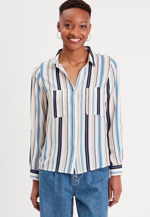 Blusa a righe in beige, blu e navy; con bottoni, maniche lunghe e due tasche sul petto; tessuto leggero con una texture liscia.