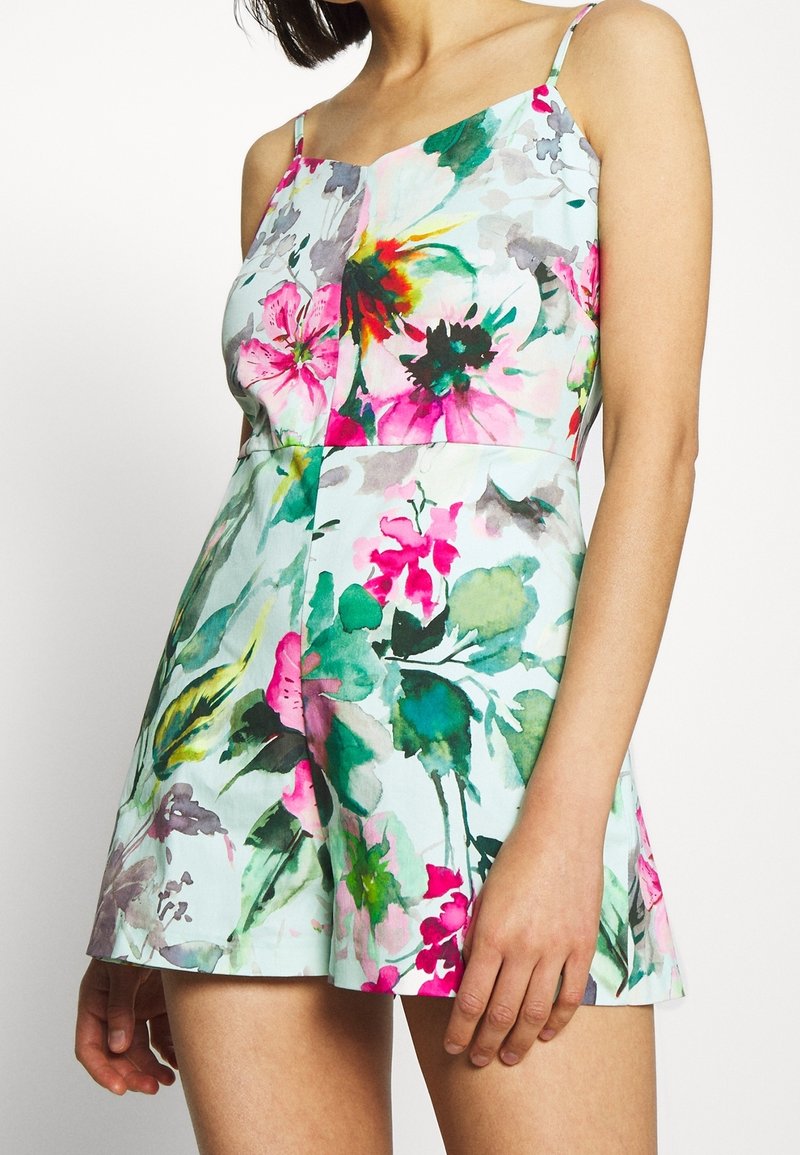 Combinaison fleurie avec un fond bleu clair, des bretelles spaghetti réglables et une coupe fluide aux teintes vives de rose et de vert.