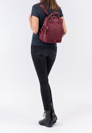 Bordowy plecak z podwójnymi uchwytami u góry i regulowanymi szelkami, z kieszeniami zapinanymi na zamek z przodu oraz gładkim, trwałym materiałem.