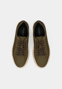 Olivgröna mockasneakers med bruna snören, rund tå och ljus gummisula. Logotyp syns på innersulorna.