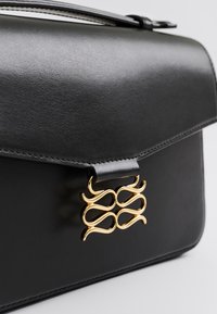 Μαύρη δερμάτινη τσάντα με λεία υφή, με χρυσό μεταλλικό κλιπ. Η τσάντα έχει δομημένο σχήμα και κομψό κλείσιμο με επικάλυψη.