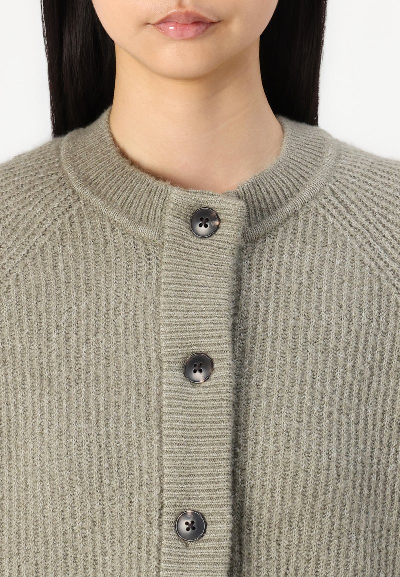 Hellgrauer gestrickter Cardigan mit gerippter Textur, Rundhalsausschnitt und vier schwarzen Knöpfen auf der Vorderseite.