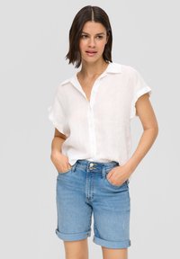 Biała koszula buttons-up wykonana z lekkiego materiału, podwinięte rękawy, w połączeniu z jasnoniebieskimi szortami dżinsowymi, złożonymi na mankietach, w luźnym kroju.