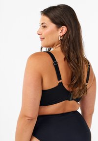 Melnas bikini augšdaļas ar regulējamiem siksniņām, aizdari un gludu tekstūru. Aizmugurējais skats uzsver elegantu dizainu un atbalstošu piegulšanu.