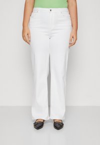 Jeans blancos de pierna ancha con bolsillos frontales, cierre de botón y una textura suave. Combinados con unos zapatos planos negros de punta afilada.