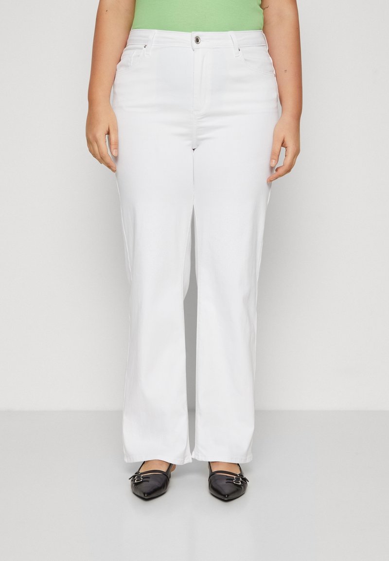 Jeans blancos de pierna ancha con bolsillos frontales, cierre de botón y una textura suave. Combinados con unos zapatos planos negros de punta afilada.