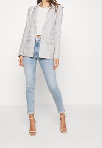 Ljust grå rutigt kavaj med skräddarsydd passform, två framfickor, i kombination med ljusblå smala jeans och kroppsnära klackar i nude.