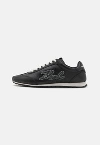 Black leather sneaker with white laces and embroidered 'Karl' logo on the side. Features a rounded toe and textured rubber sole.
