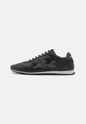 Svart lær sneaker med hvite snørebånd og broderte 'Karl'-logo på siden. Har rund tå og teksturert gummisåle.