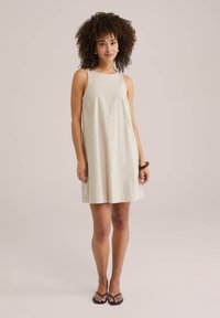 Rochie fără mâneci, de culoare bej deschis, realizată dintr-un material moale. Formă A-line cu o textură fină și un finisaj subtil la margine. Purtați-o cu sandale negre.