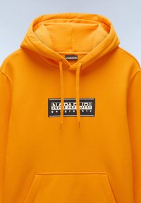 Oranje sweatshirt met een capuchon, voorzien van een zwart rechthoekig logo met de tekst "NAPAPIJRI geographic." Inclusief een zak aan de voorkant en een gestructureerde stof.