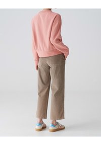 Felpa rosa con una vestibilità rilassata, pantaloni ampi beige e sneakers bianche con accenti blu e rossi. Tessuto morbido, design minimale.