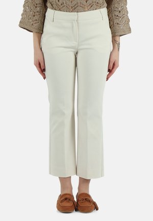 Donna che indossa un maglione beige all’uncinetto, pantaloni dritti color avorio e mocassini marroni, in piedi con le mani rilassate lungo i fianchi.