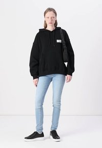 Sweat à capuche noir oversize avec poche frontale et cordon de serrage, associé à un jeans skinny bleu clair et des baskets noires avec semelles blanches.