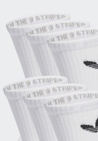 Baltas sporta zeķes ar ribotu tekstūru, izsistītu logotipu un frāzi "THE 9 STRIPED" augšējā malā.