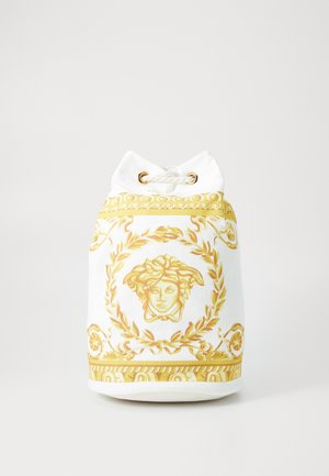 Sac blanc à cordon avec un motif doré orné de tête de Méduse et une couronne de laurier sur le devant, posé sur un fond uni.