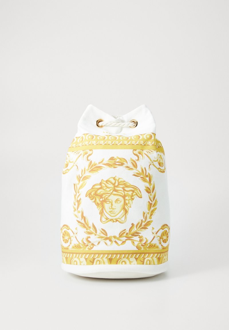 Sac blanc à cordon avec un motif doré orné de tête de Méduse et une couronne de laurier sur le devant, posé sur un fond uni.