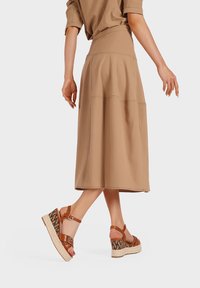Gonna midi marrone con dettagli cuciti abbinata a sandali con zeppa color cammello, caratterizzati da un motivo intrecciato e suola in stile espadrilles.