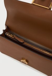 Bolsa de mão de couro castanho com uma textura suave, apresentando um bolso com fecho de zip e um fecho de clasp em tom dourado. Interior em cor contrastante.