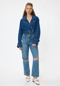 Chaqueta de mezclilla con cuello de muesca y diseño de doble botonadura, combinada con jeans de pierna ancha desgastados. Tejido azul claro con una textura suave.