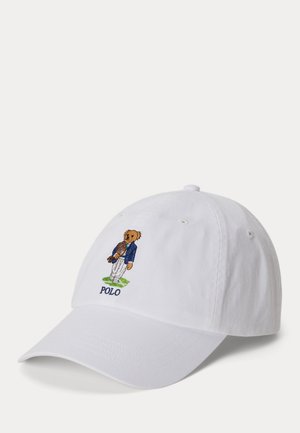 Hvid baseballkasket med broderet bamse i blå jakke, der holder en polo-hjelm, stående på grøn græsplæne med teksten "POLO" nedenunder.