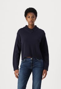 Pull cropped marine avec un col en V et un ourlet ribbed, en matière douce, associé à un jean en denim bleu.