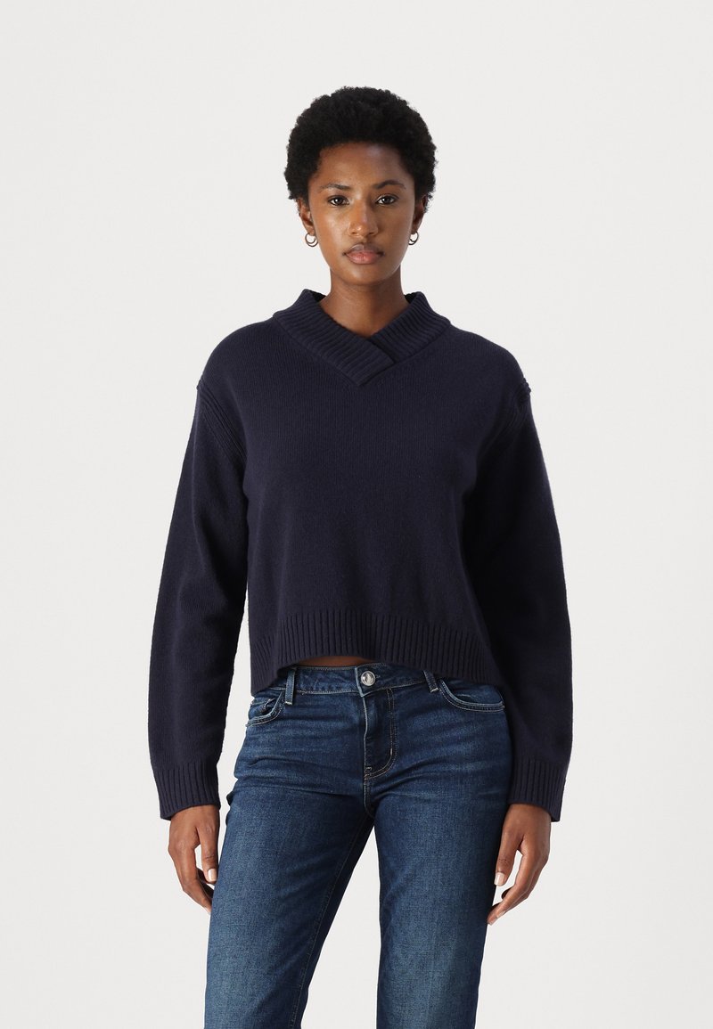 Pull cropped marine avec un col en V et un ourlet ribbed, en matière douce, associé à un jean en denim bleu.