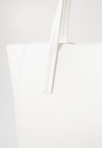 Hvid tote bag lavet af tekstureret syntetisk materiale, med lange håndtag og et minimalistisk design med synlige syninger.