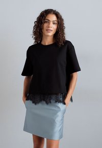 Μαύρο μπλουζάκι κοντομάνικο με δαντέλα, συνδυασμένο με ανοιχτό μπλέ σατέν φούστα. Η μπλούζα έχει άνετη εφαρμογή, ενώ η φούστα είναι εφαρμοστή.