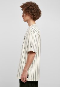 Cremefarvet kortærmet t-shirt med sorte lodrette striber, løs pasform, syninger og logodetalje på venstre side.