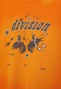 Deux cow-boys chevauchant des taureaux, entourés d'étoiles et du texte « La division » sur un fond orange.