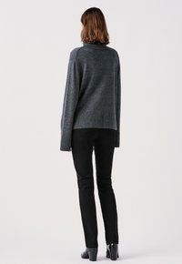 Grijze gebreide trui met een hoge hals en geribde manchetten, gecombineerd met zwarte slim-fit pantalons en zwarte hakken.