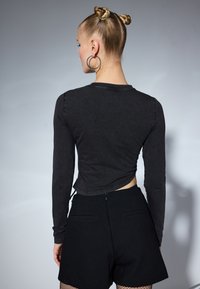 Svart langermet topp med en cropped fasong og rund hals, kombinert med høyt liv shorts i svart. Har en knyttet detalj bak.