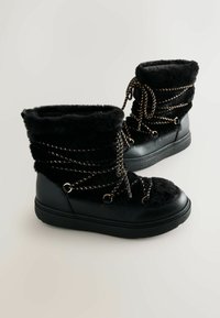 Schwarze Stiefel mit einem weichen Obermaterial aus Kunstfell, Kunstlederakzenten und metallischen Schnürsenkeln. Runde Zehenpartie und flache Gummisohle.
