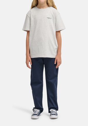 Bambino che indossa una maglietta grigio chiaro Element Co., pantaloni blu scuro e sneakers blu navy con lacci bianchi, in piedi contro uno sfondo semplice.