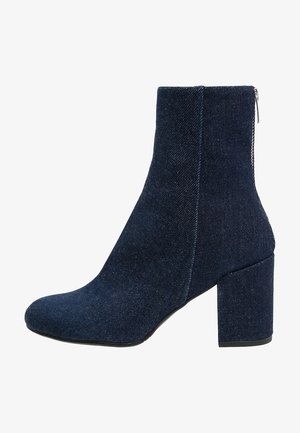 Bottines en denim avec un talon bloc, fermeture éclair et une couleur bleu foncé. Texture lisse avec une silhouette effilée et des détails de design minimalistes.