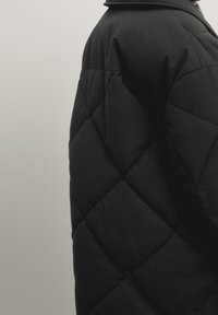 Zwarte gewatteerde pufferjas met een matte afwerking, voorzien van een hoge kraag en een ruitpatroon over de stof.