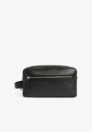 Trousse de toilette rectangulaire en cuir noir avec une poche zippée à l'avant et une sangle de poignée latérale sur fond blanc.