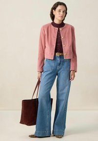 Veste cropped en velours côtelé rose avec des boutons dorés, associée à un jean en denim bleu à taille haute et jambes larges, et un sac fourre-tout en suede bourgogne.